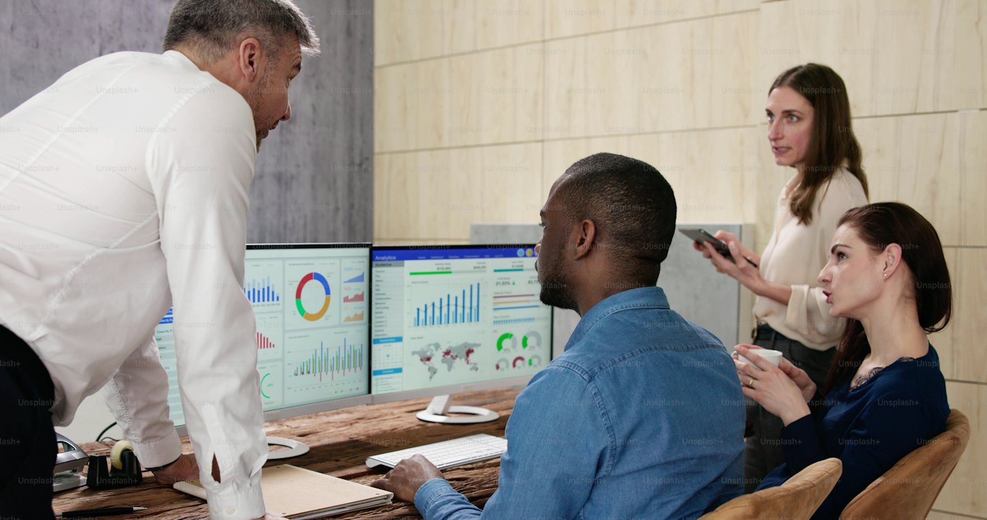 Profesionales de negocios colaboran analizando datos en monitores de computadora.